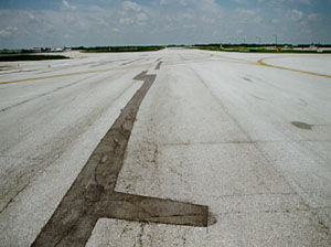 Overview of a long, narrow, wandering patch at the centerline of a taxiway pavement.              There is noticeable cracking within the patch area.