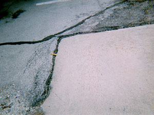 Overview photo showing an asphalt surface around the corner of a PCC slab.            The asphalt at the joint between the PCC and asphalt surfaces is noticeably higher than the PCC slab.