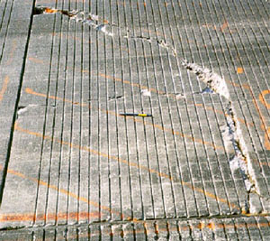 Close-up photo of a PCC slab corner with a high-severity corner break. The corner break is broken into two pieces, has considerable spalling, and has noticeable faulting.