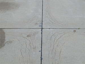 Close-up photo showing a corner where four PCC slabs come together.  All four slab corners           in the photo show a series of crescent-shaped D-cracks.  The cracks are all tight with no visible spalling.