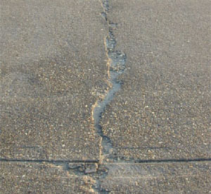 Close-up photo of a single high-severity crack in a PCC slab.  The crack appears to be greater than 1 in (25 mm) wide           and shows areas of spalling with high FOD potential.
