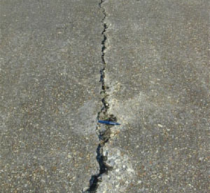 Close-up photo of a single medium-severity crack in a PCC slab.  The crack appears to be 1/2 in (13 mm) wide           and shows areas of spalling.