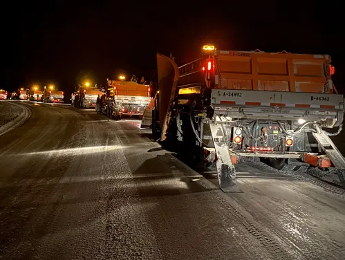 Line of snowplows moving snow at night