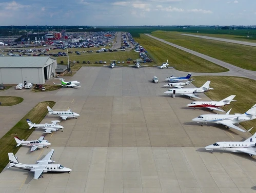 Business jets and private planes sit on a large patch of cement at an airport
