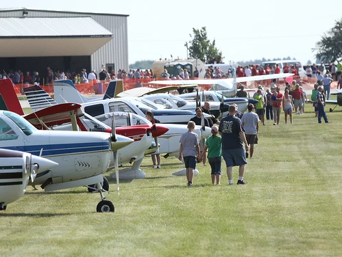 Airplanes sit in a grassy area for an air show, with visitors walking by