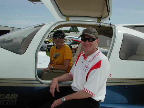 A woman sits in the cockpit of a small-engine plane, with a man standing outside the door smiling