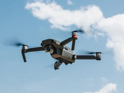 A black drone (unmanned aircraft) hovers with four propellers against a blue sky