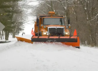 Photo of an orange Iowa DOT Snowplow, plowing snow on a road.