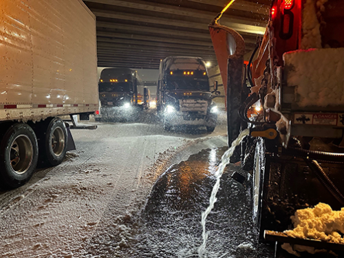 an Iowa DOT snowplow truck releasing brine on a dark winter highway