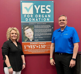 two people standing next to a poster about being an organ donor