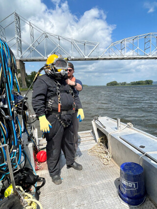 A diver in diving equipment, standing on the deck of a boat, preparing to enter the river.