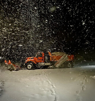 photo of a snowplow at night with snow coming down and on the road
