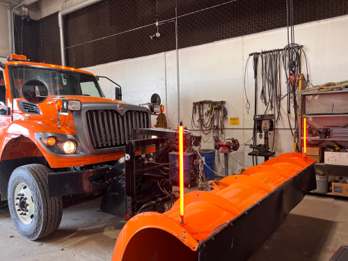tall, thin, orange lights attached to the front edges of a snowplow