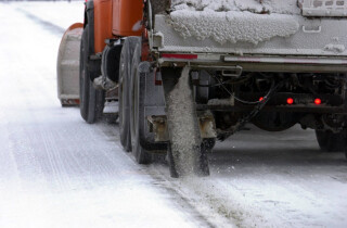 the back end of a snowplow as it applies salt to a snowy road