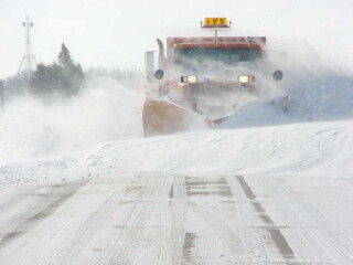 the front of a snowplow truck plowing snow on a wintery road