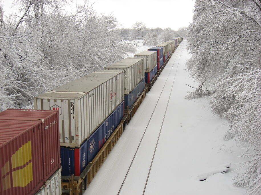 Container cars double staked on freight railroad cars traveling down the tracks in snow