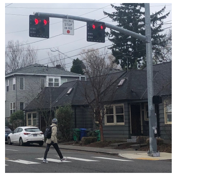 Photo of a pedestrian hybrid beacon with two red lenses and one yellow lens controlling a marked crosswalk as pedestrians cross.