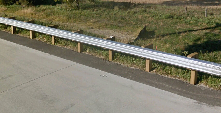 Steel beam guardrail installed along a roadway with posts and blockouts.