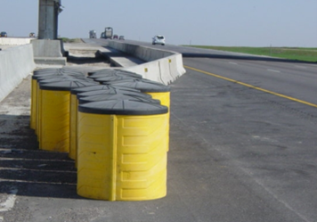 Sand‑filled barrel array placed in front of a roadside obstacle.