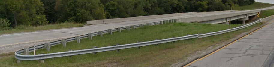 Side view of a U‑shaped bullnose guardrail in a median, showing curved rail sections connected to straight approach rails.
