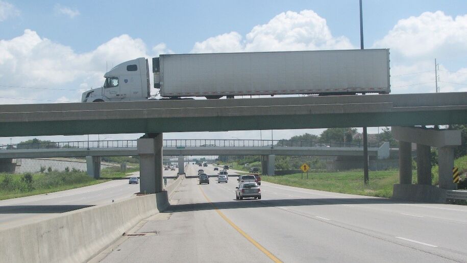 Permanent concrete barrier rail on a highway beneath an overpass with traffic in both directions.