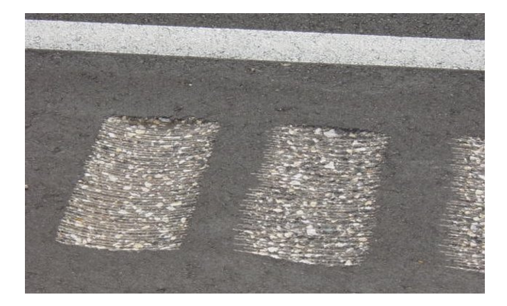 A close‑up photo of milled rumble strips cut into asphalt beside a white edge line.