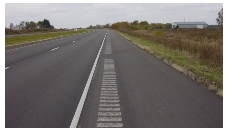 A rural paved road with shoulder rumble strips showing a repeating pattern of rumble segments and a 12‑foot gap.