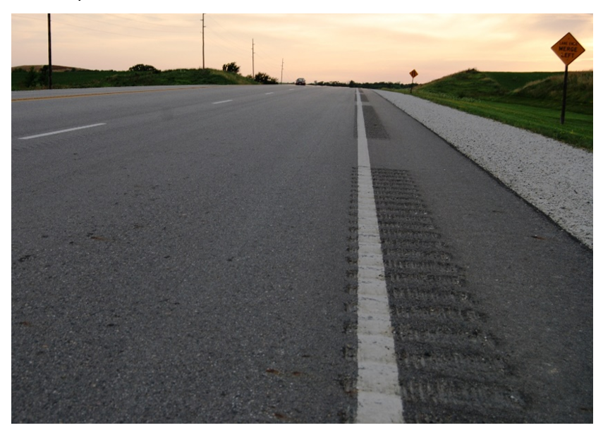 A roadway at sunset with rumble stripes cut into the shoulder beside a white edge line.